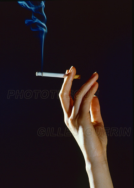 Jolie main de femme tenant un cigarette allumée entre le majeur et l'index et volutes de fumée bleutée