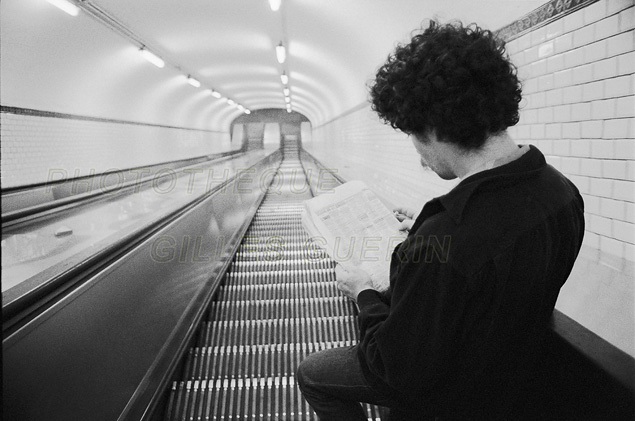 Jeune homme lisant les annonces du journal dans un escalier mécanique du métro parisien - 1979